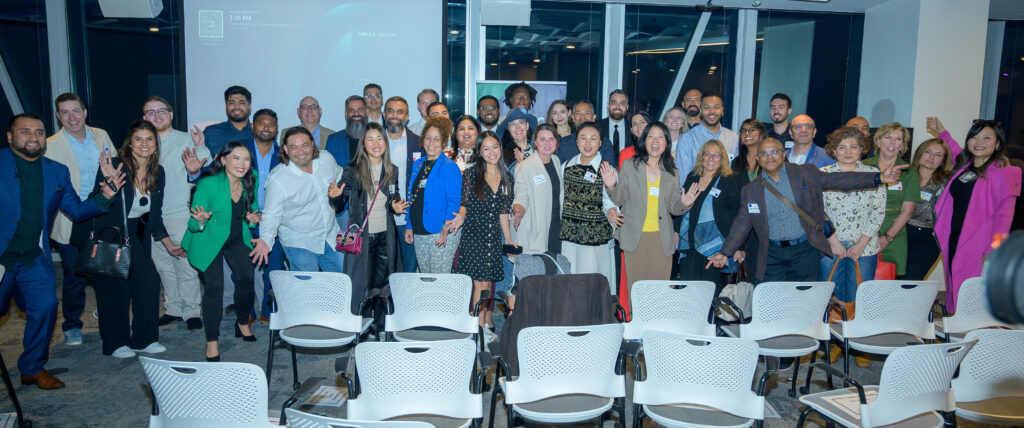 A large group of people pose together, smiling in a conference room.
