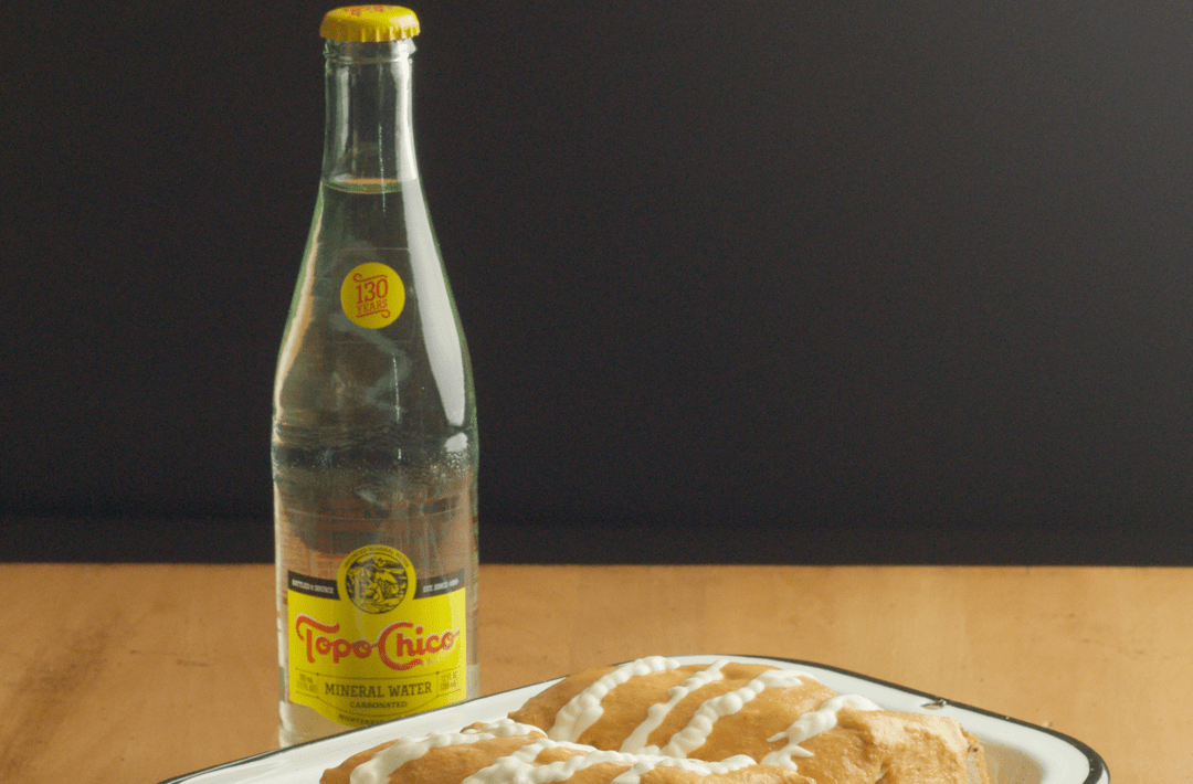 A sandwich on a tray next to a glass bottle of Topo Chico.