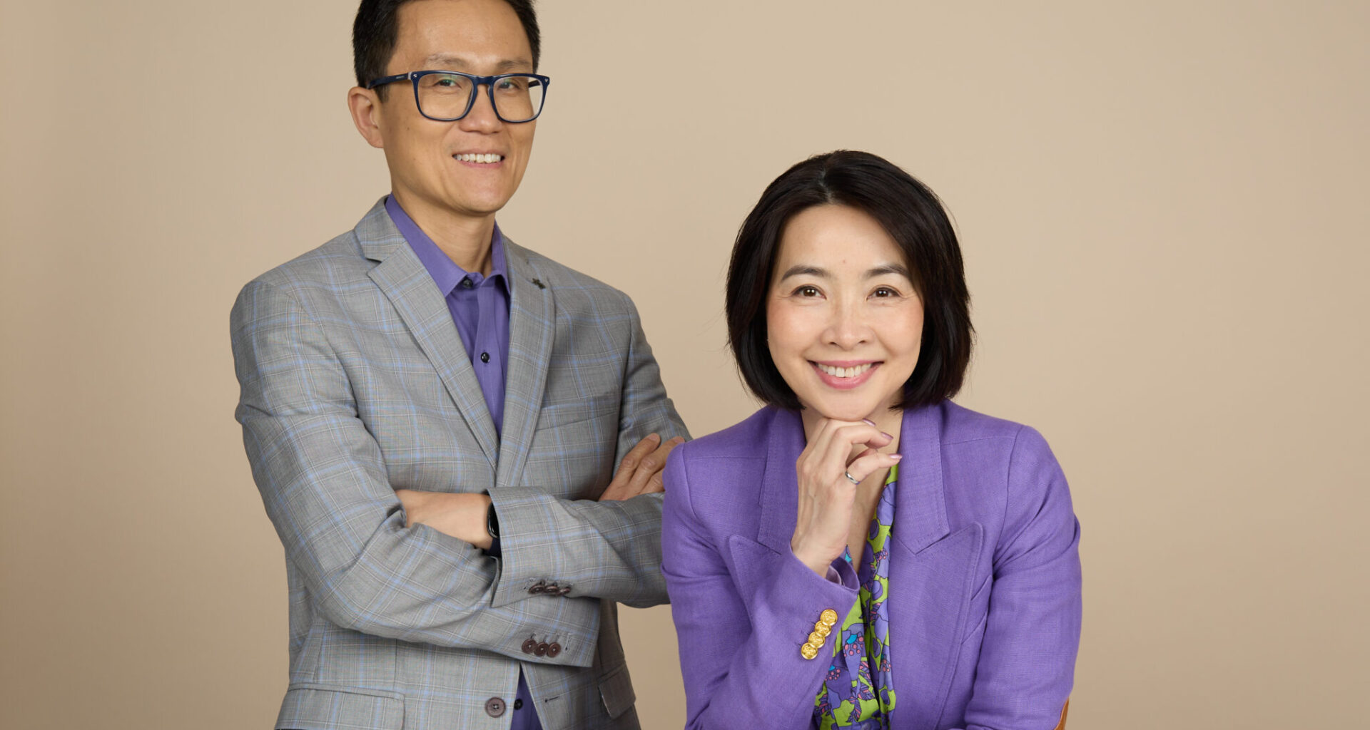 Allen stands beside Eva who is seated at the table. They are smiling at the camera.