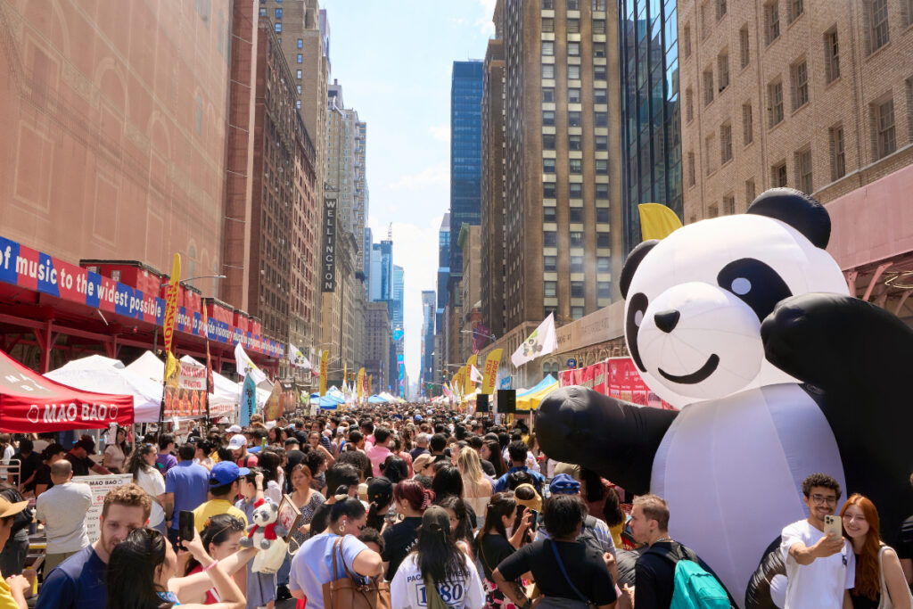 Image shows downtown streets with attendants of Panda Fest with an inflatable panda at right of screen.