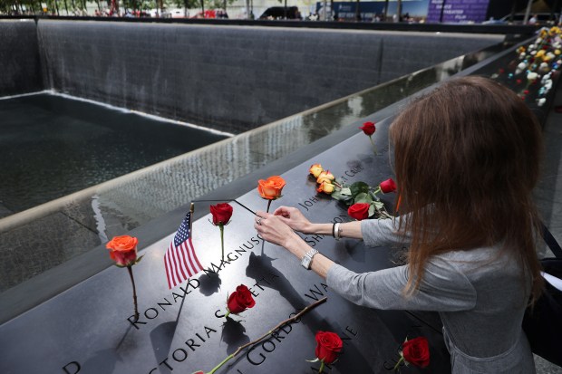 Sheryl Magnuson places a flower in her father's name where it is inscribed on the National 9/11 Memorial south pool following the commemoration ceremony at the memorial on September 11, 2021 in New York City. (Photo by Chip Somodevilla/Getty Images)
