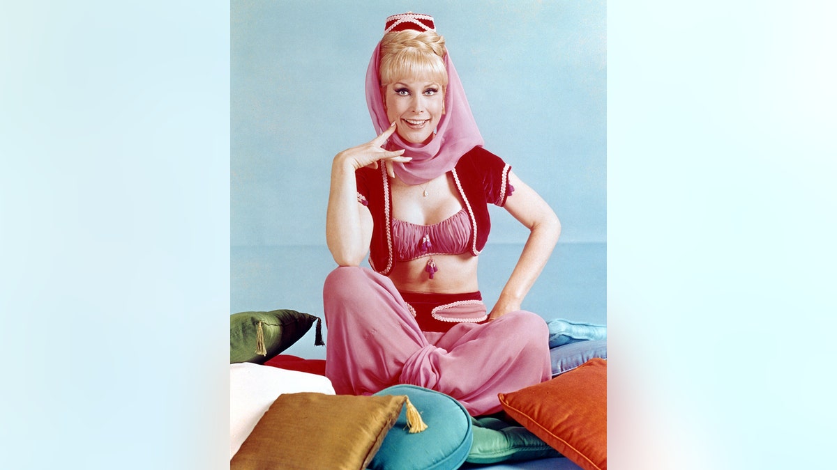 Barbara Eden in costume sitting on a multi-colored pile of cushions.