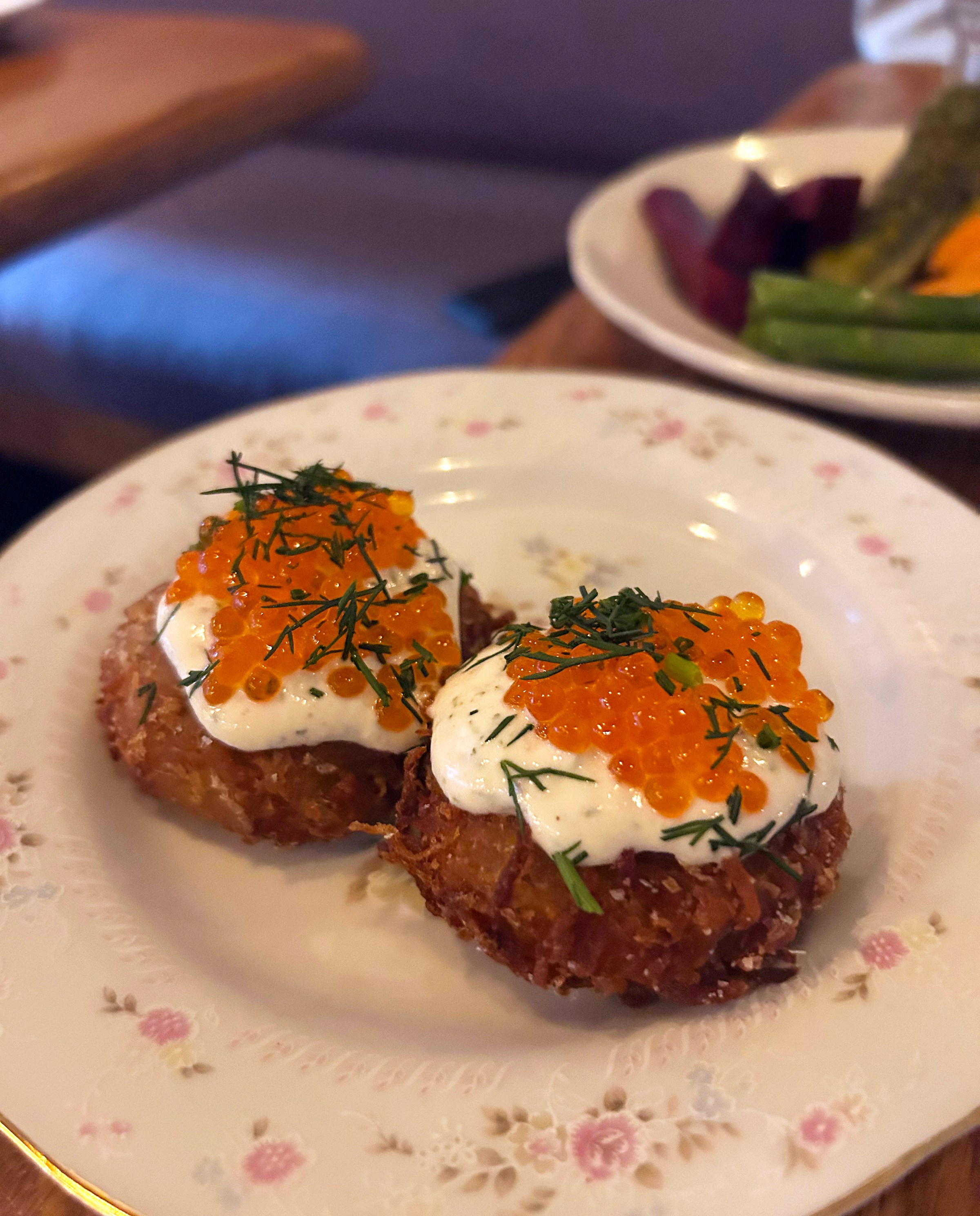 Two latkes with white cream and orange roe eggs and green herbs on a plate.