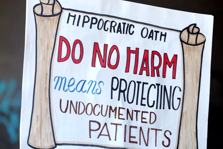 A sign resembling a scroll states, "Hippocratic Oath: Do No Harm means Protecting Undocumented Patients."