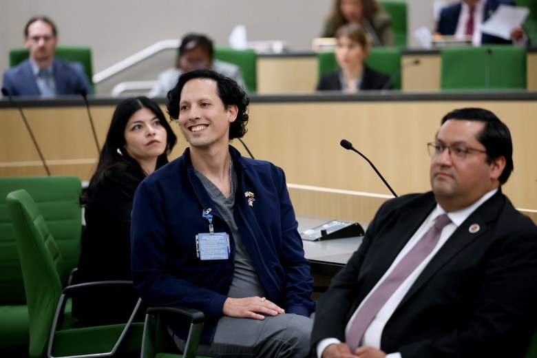 People sitting in a formal meeting with green chairs and microphones.