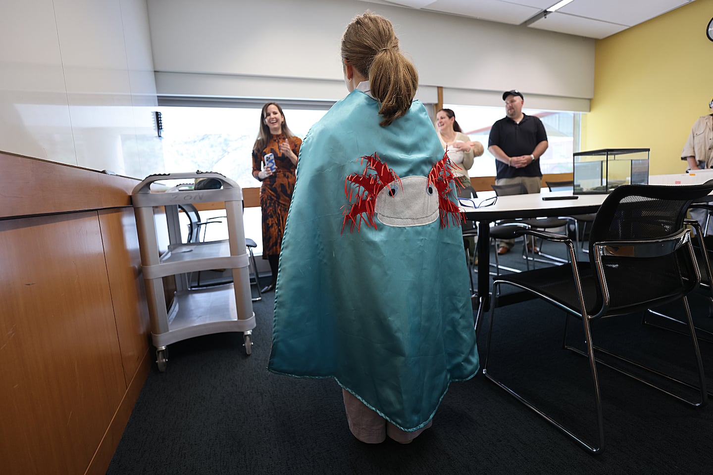 At the Harvard Department of Stem Cell and Regenerative Biology, Marianne Cullen, 6, gets to wear a cape with an axolotl on it as lab director Jessica Whited (left) looks on.