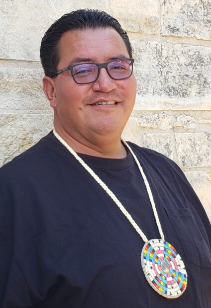 A portrait of Matthew Davila, smiling in glasses and wearing a circular beaded necklace.