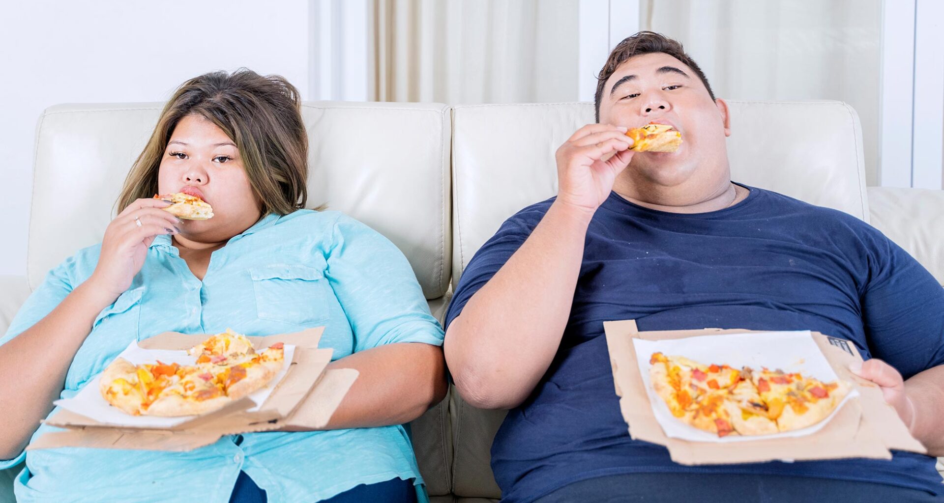 Obese Couple Eating Pizza on Sofa