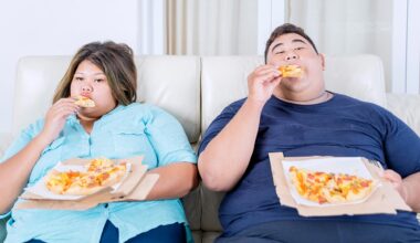 Obese Couple Eating Pizza on Sofa