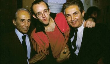 Two gentlemen in suits with a young bespectacled man in red.