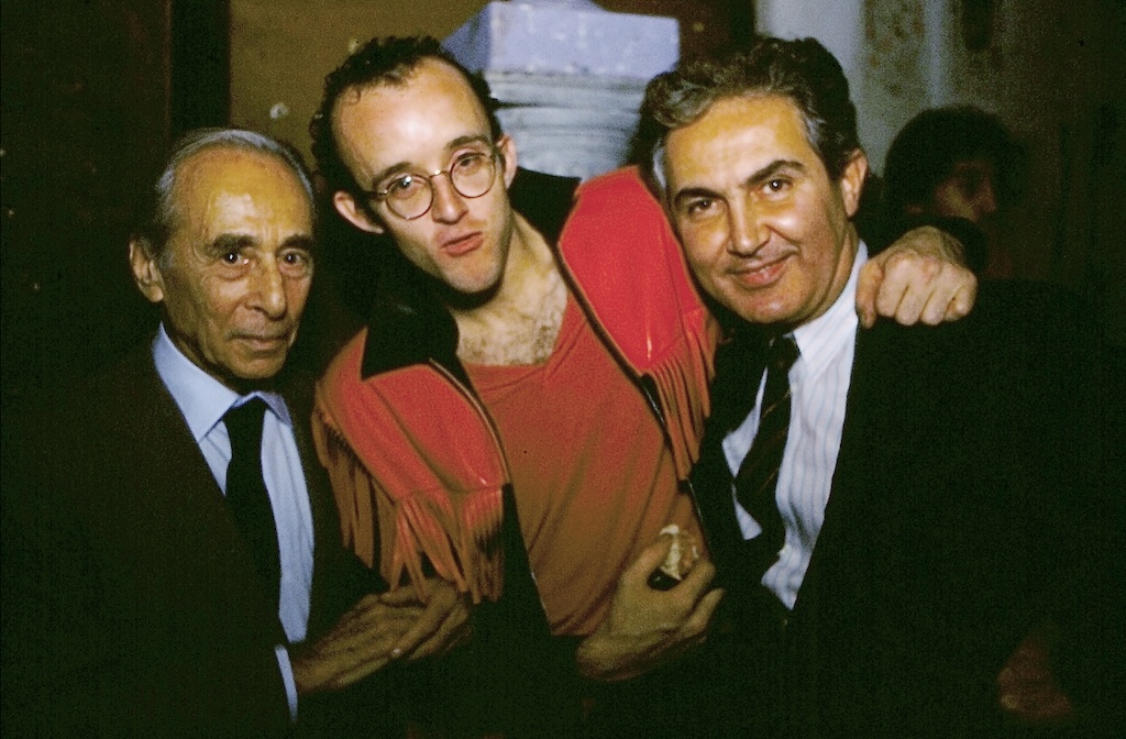 Two gentlemen in suits with a young bespectacled man in red.
