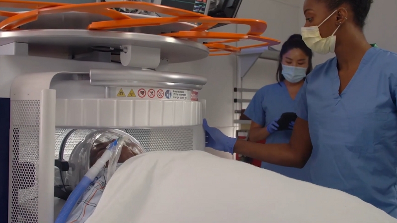 A patient undergoes a scan with a portable ultra-low-field MRI as healthcare workers monitor the procedure