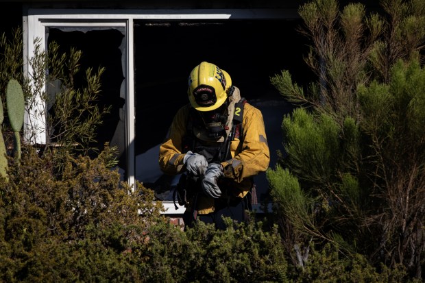 Blown out windows are shown as a firefighter fixes their gloves as they work to put out a fire at Monterey Mobile Lodge. (Ana Ramirez / The San Diego Union-Tribune)