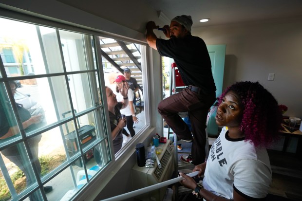 Eric Allidem and Danii Veney, in the final hour before the Day of Joy, install a curtain rod in Heather Moore's living room. The design team from Humble Design San Diego and volunteers have been working since the morning to furnish Moore's home on Friday, Aug. 15, 2025, in La Mesa, CA.  (Nelvin C. Cepeda / The San Diego Union-Tribune)