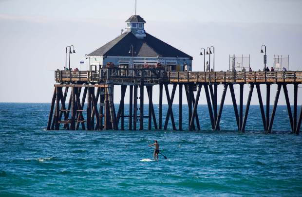 Paddle boarder passing the Imperial Beach Pier in Imperial Beach...
