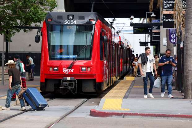 People walk past a Blue Line trolley at the 12th and Imperial Transit Center on Friday, May 30, 2025 in San Diego. (Meg McLaughlin / The San Diego Union-Tribune)