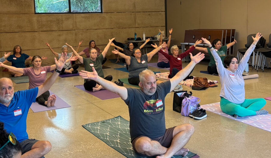 Group participants in a morning yoga class on mats with hands raised above their heads.