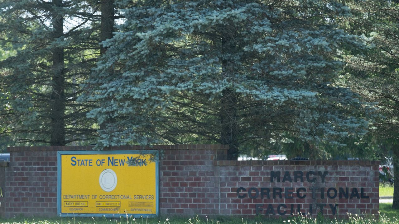 marcy correctional facility and doccs signs on low brick wall, pine trees behind them, at daytime