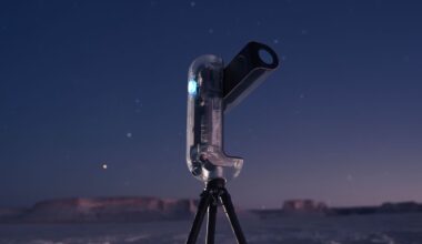 A modern, transparent telescope on a tripod stands outdoors at dusk, with a clear sky and distant mesas in the background. Stars are visible in the sky, and the scene has a calm, twilight atmosphere.