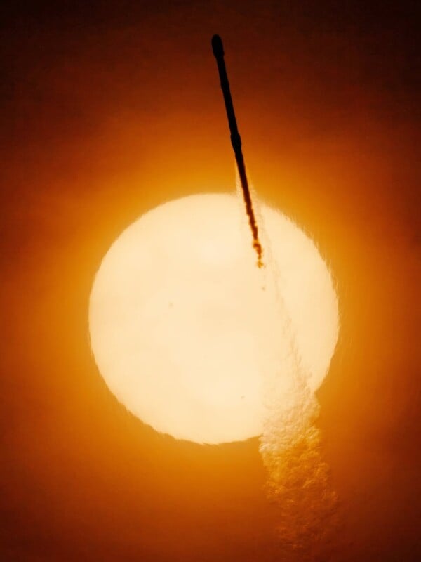 A rocket is launching into the sky with a bright, glowing sun in the background, casting an orange and yellow hue across the scene while the rocket's exhaust trail is clearly visible.