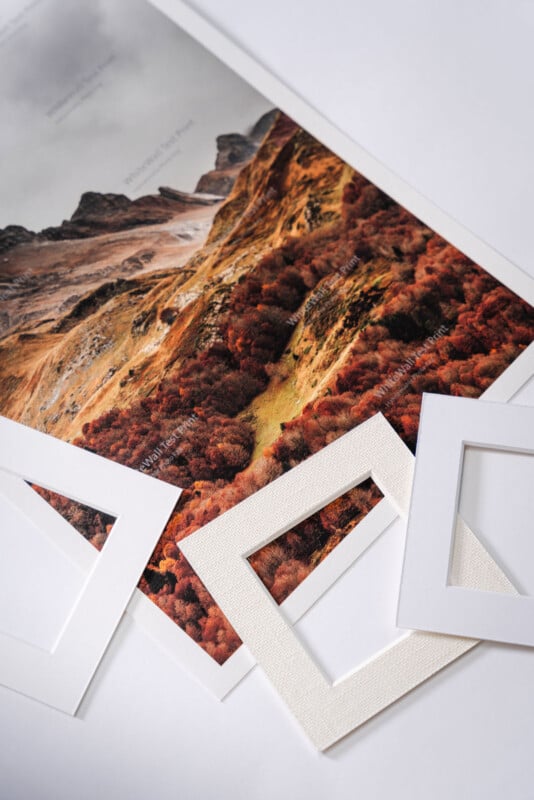 A photo print of a rocky, autumn-colored landscape is placed on a white surface, surrounded by two white rectangular picture mat frames.