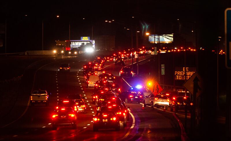 Lines of cars, their red tail lights glowing, wait to enter the NYS Fairgrounds at night.