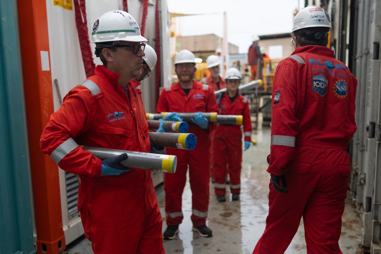 A group of uniformed workers wearing hard hats hold cylindrical tubes.