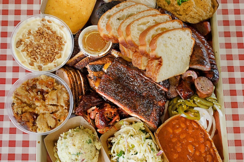 A platter with brisket, sausage, turkey, ribs, homemade brioche, sides and desserts is seen...