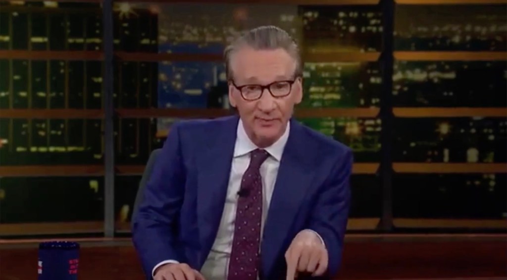 Bill Maher in a suit and tie on a television set.