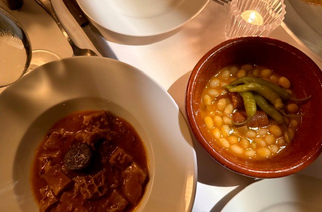 One bowl of red stew next to a plate of yellow beans.