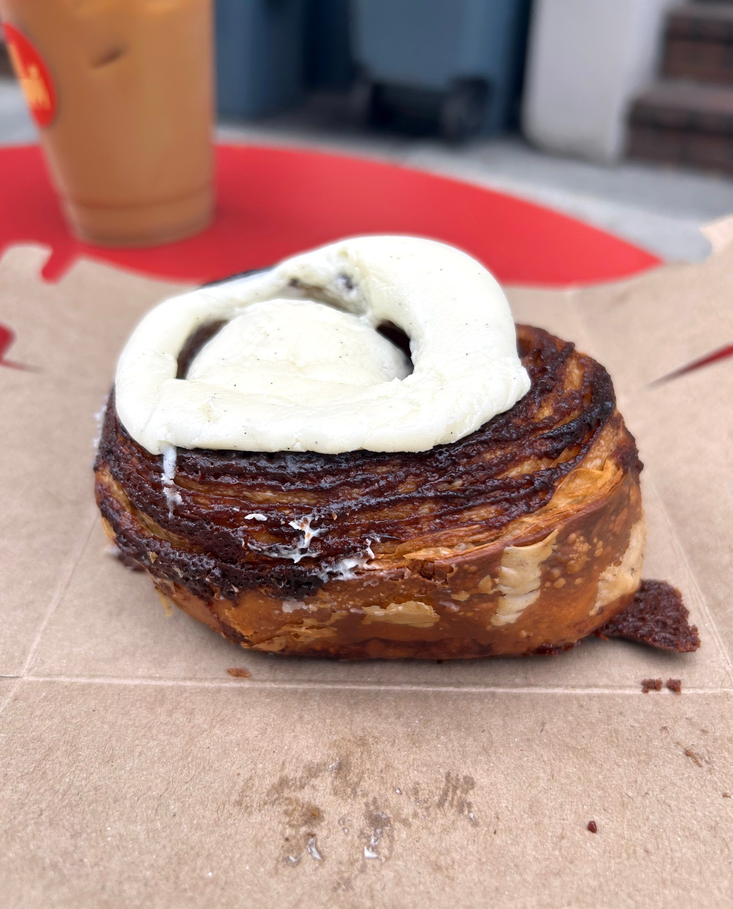A cinnamon bun with white frosting on a box outside.