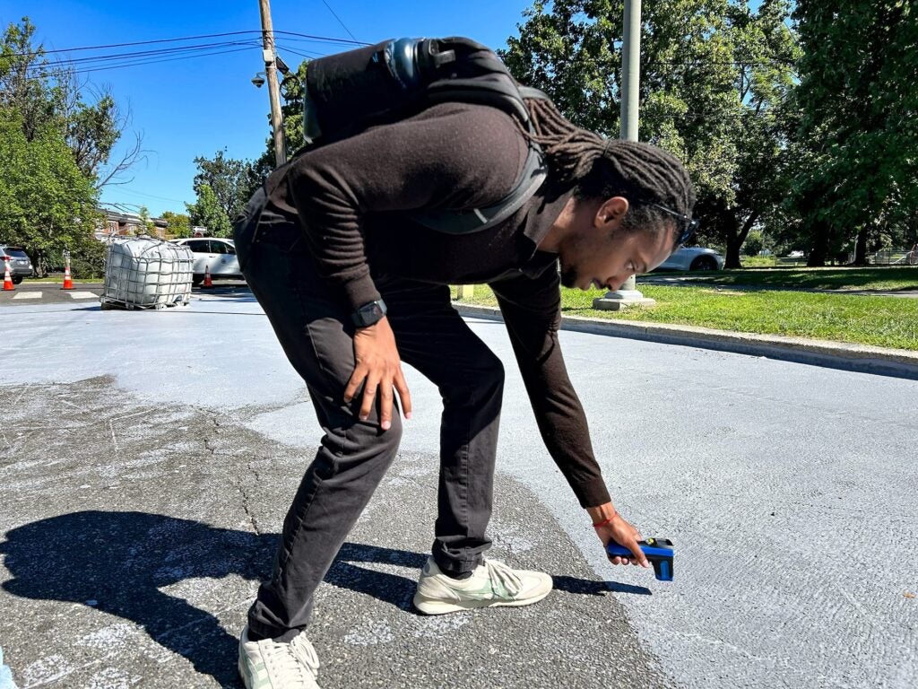 A man leans down to test the temperature of a coated portion of the street