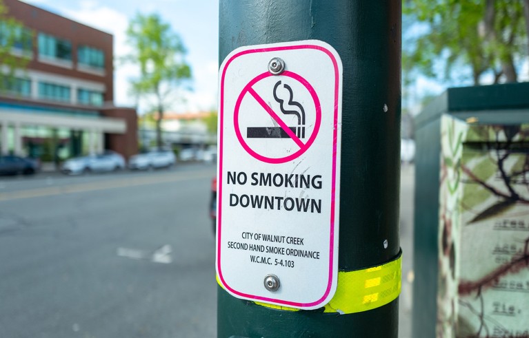 Sign attached to a street post indicating a no smoking district in a downtown area in California.