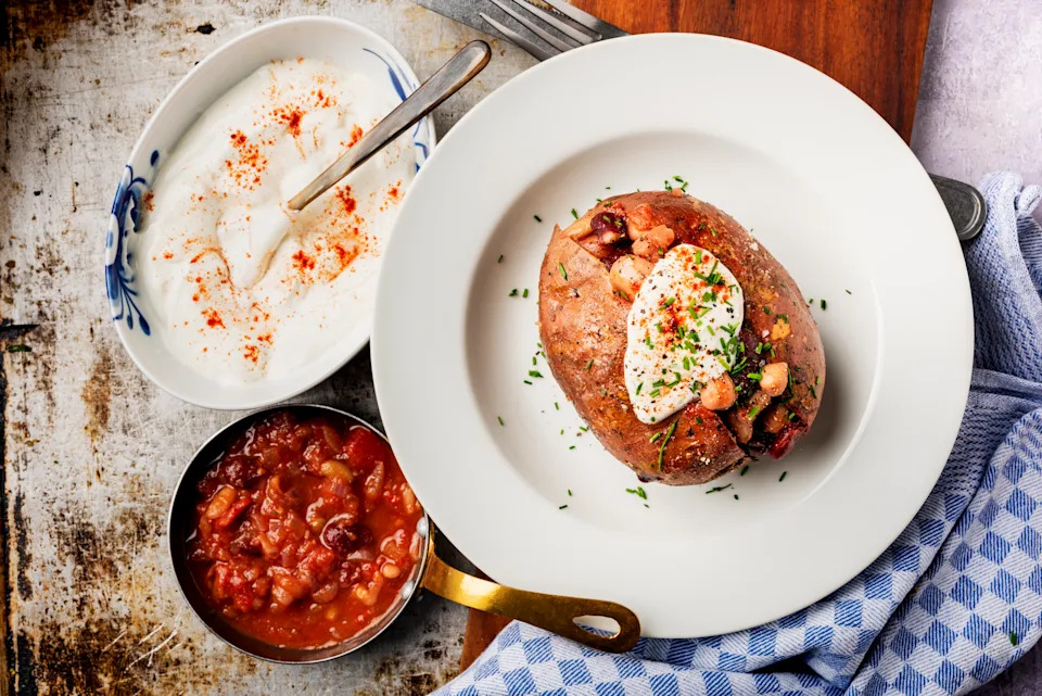 Roasted sweet potato filled with kidney beans, lima beans and chickpeas, served with a sour cream dressing with smoked paprika.
Roast your sweet potatoes for around 45 minutes. Meanwhile, prepare your beans by making a simple tomato sauce with red onion and garlic, and add passata. Add the packet of mixed beans. When your sweet potato is ready, cut it open, add a little butter if you wish, and fill it with the tomato and bean filling. Serve with a simple sour cream or Greek yoghurt dip, featuring smoked paprika, chilli flakes, and chives. Delicious, filling, affordable, and healthy.