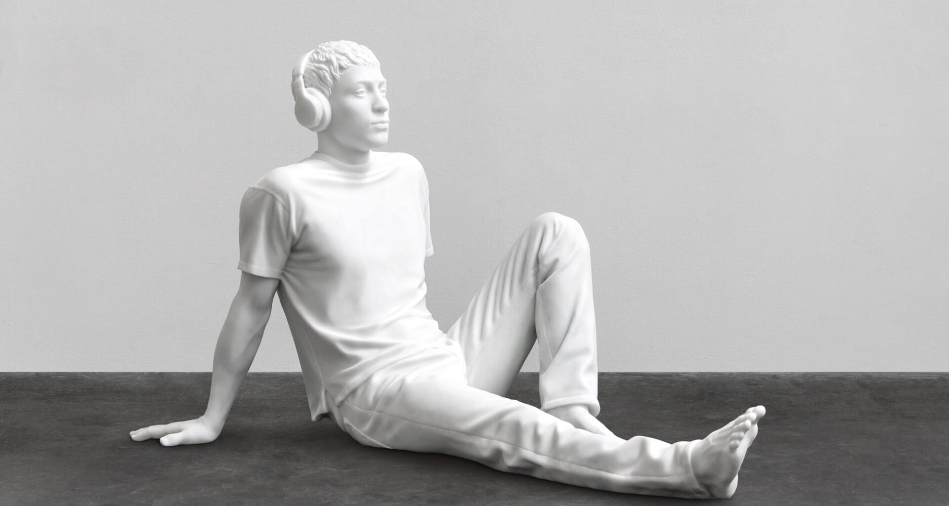 a sculpture by Elmgreen and Dragset of a white figure resting on the floor wearing headphones