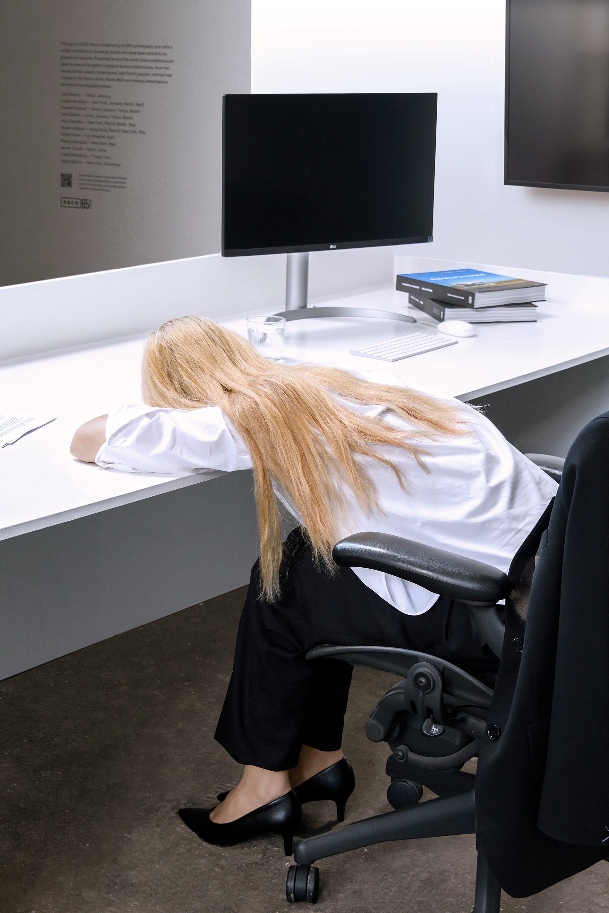 an installation by Elmgreen and Dragset of a realistic looking blond woman slumped over at her desk