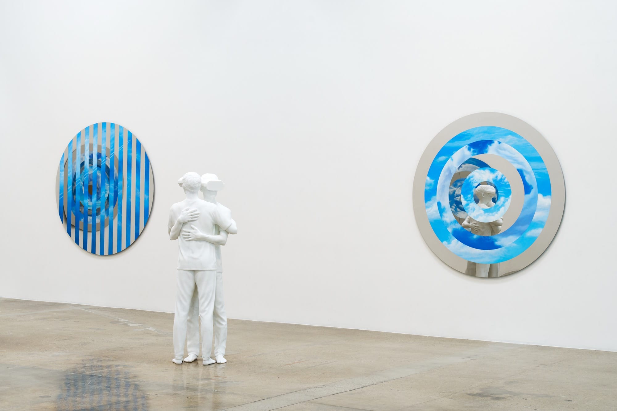 a sculpture by Elmgreen and Dragset of two figures embracing with cloud-like wall works behind