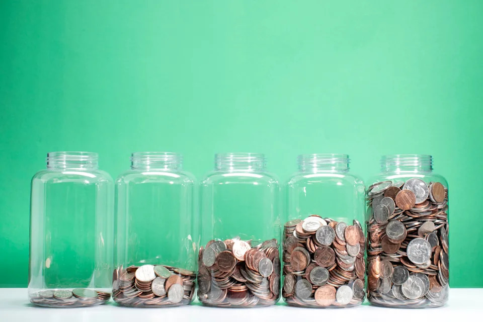 Five glass jars with increasing amounts of coins from left to right, symbolizing savings or financial growth