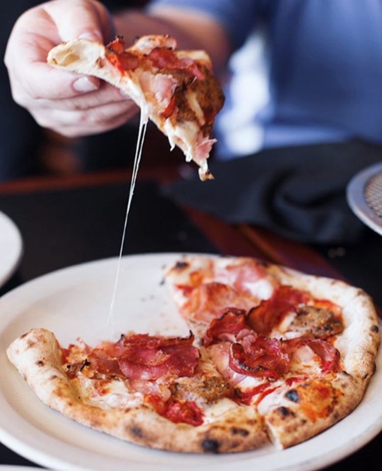 A hand pulls a slice from a pepperoni pizza.