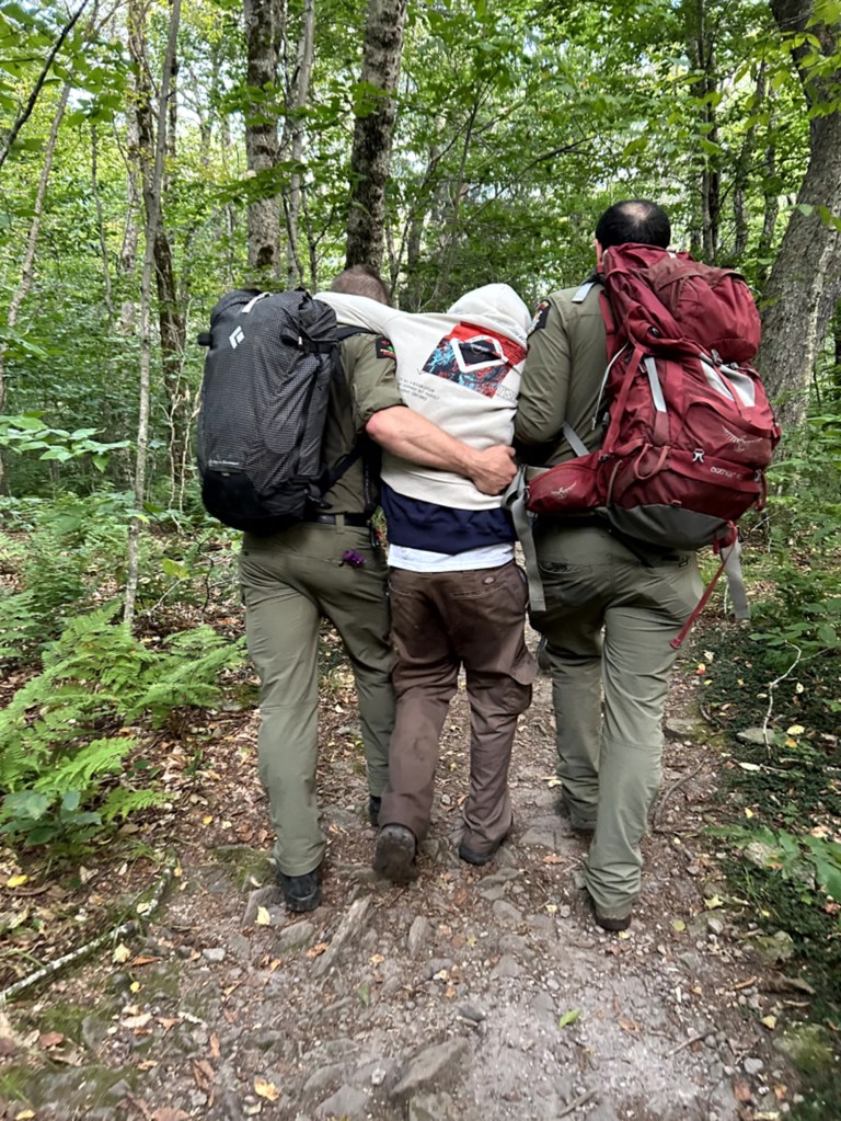Two rescuers helping a hiker walk through the woods.