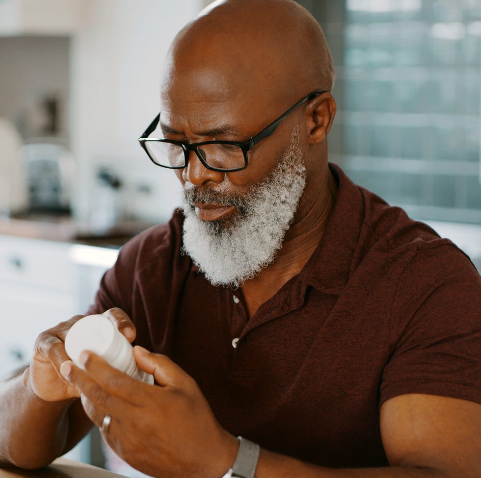 cropped shot of a senior man sitting alone in his kitchen and taking pills