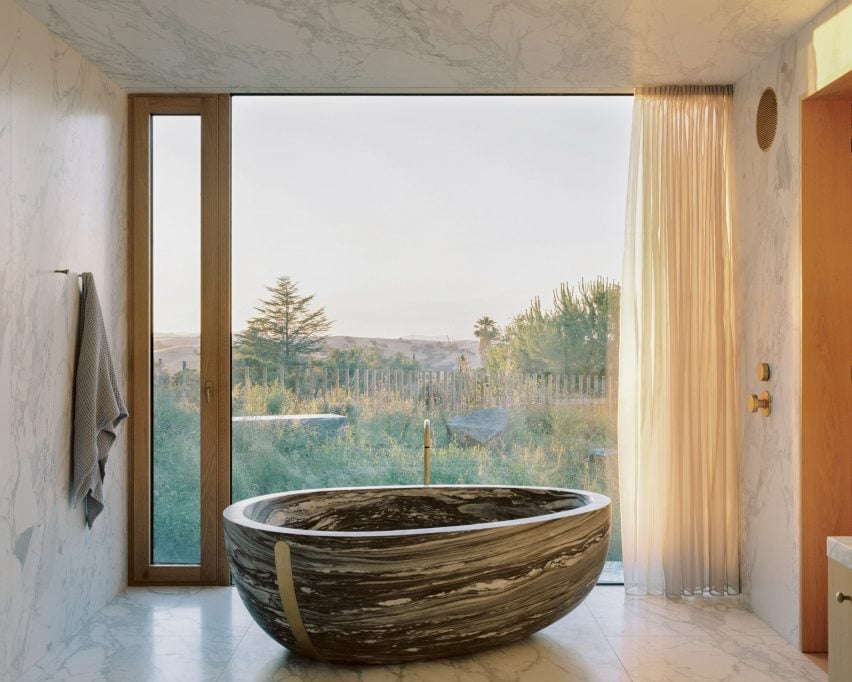 Ovoid bathtub made from dramatic marble overlooking a meadow-like garden