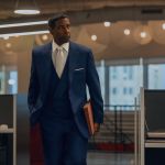 The actor Denzil Washington is wearing a navy three-piece suit, white tie and white dress shirt, holding a manilla folder while walking through an open office in a scene from Spike Lee's newest move, Highest 2 Lowest. Washington plays music tycoon David King.