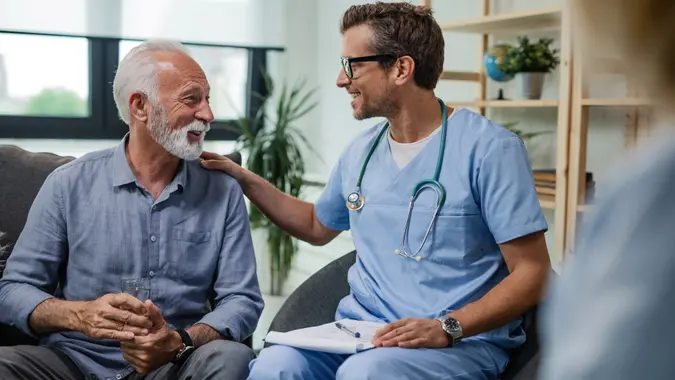 Happy doctor talking to senior male patient while being in a home visit.
