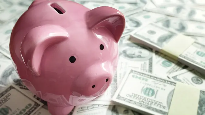 A pink piggy bank standing on top of a pile of cash.