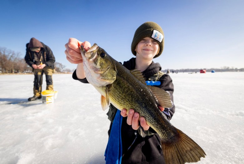 Boy smiles and holds fish on icy lake.