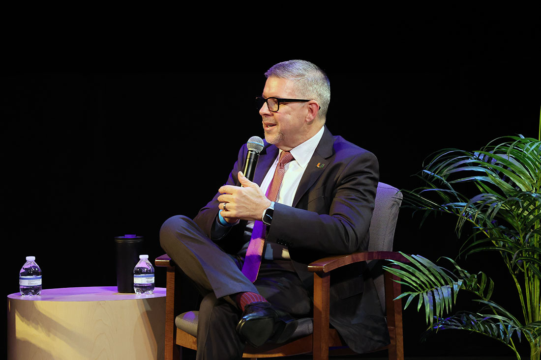 Dr. Frank Penedo speaking through a microphone onstage at the cancer summit