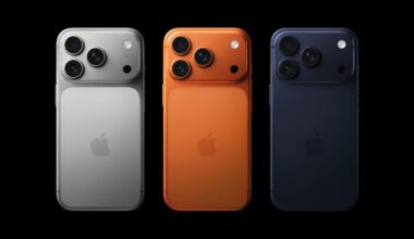 Three iPhones are shown from the back in silver, orange, and dark blue colors, each with three camera lenses and the Apple logo, on a black background.