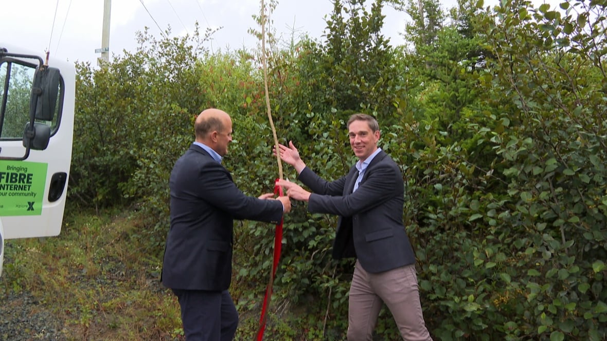 Two men wearing suits stand  in a grassy field. They have their hands around a cable rope that leads upward.