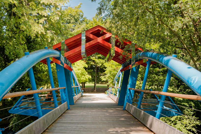 coral-toned timber and mirror canopy by GRRIZ transforms footbridge above river in france